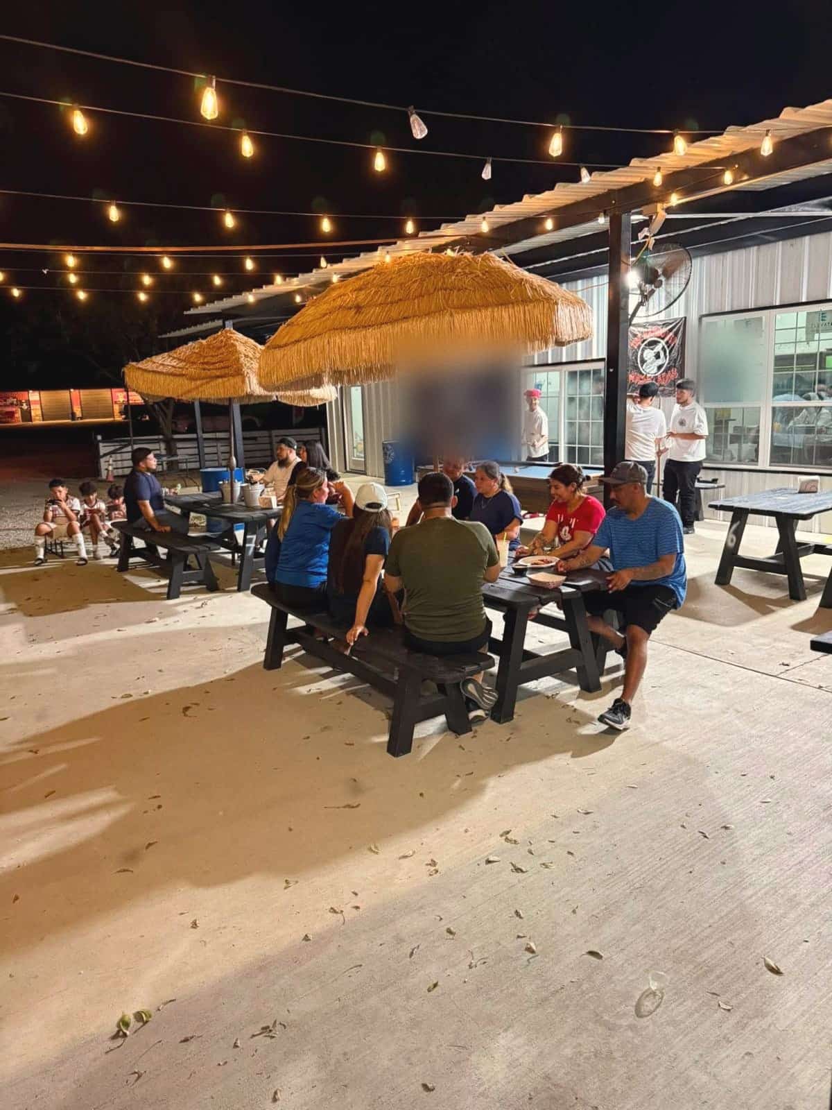 The patio at night: string lights, palapa umbrellas and families at picnic tables